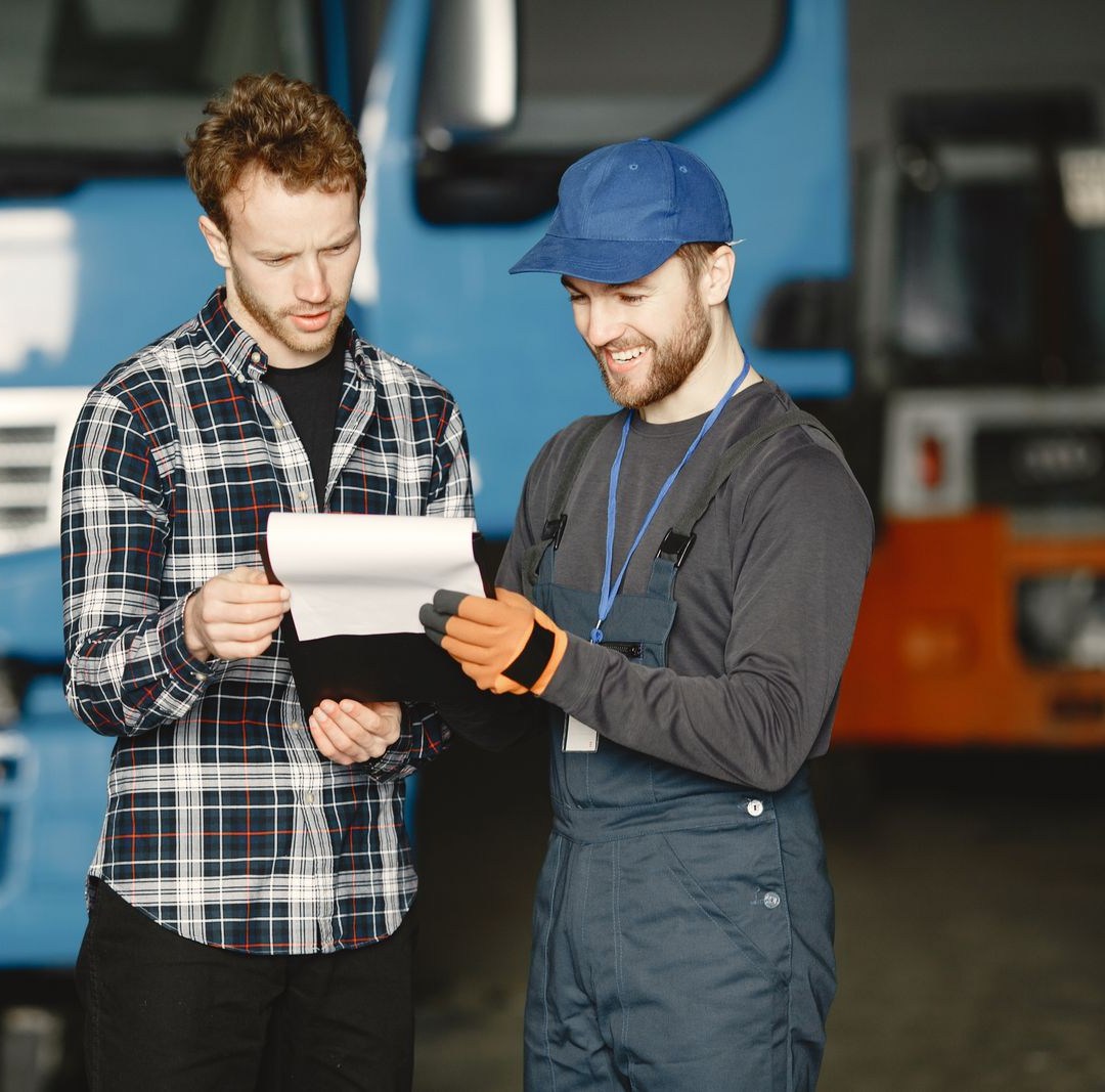 Two men reviewing a clipboard in front of work trucks